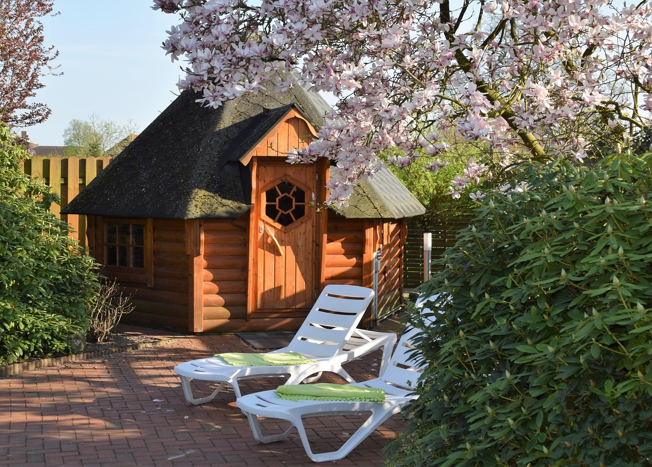 Traditional cedar sauna cabin in a landscaped backyard garden with lounge chairs — completed Cedar & Steam installation